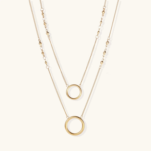 Layered gold necklace set with two open circle pendants and mixed chain styles on beige background