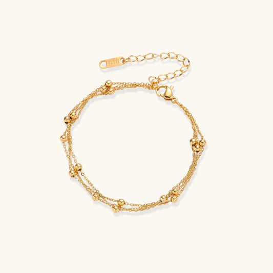 Three-strand gold-plated bracelet with clustered ball beads and adjustable clasp on cream background